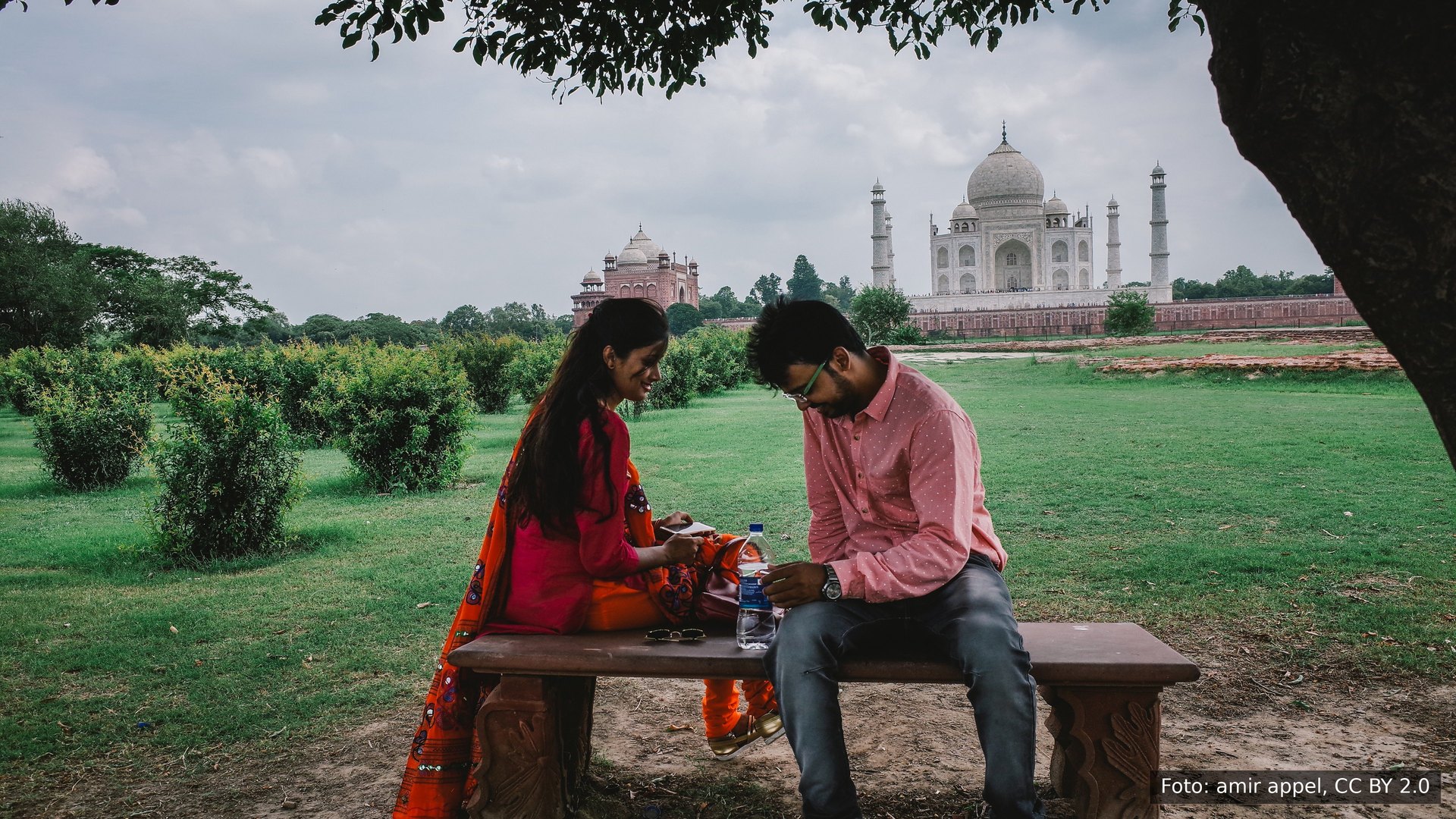 Um jovem casal em um banco nos jardins em frente ao Taj Mahal