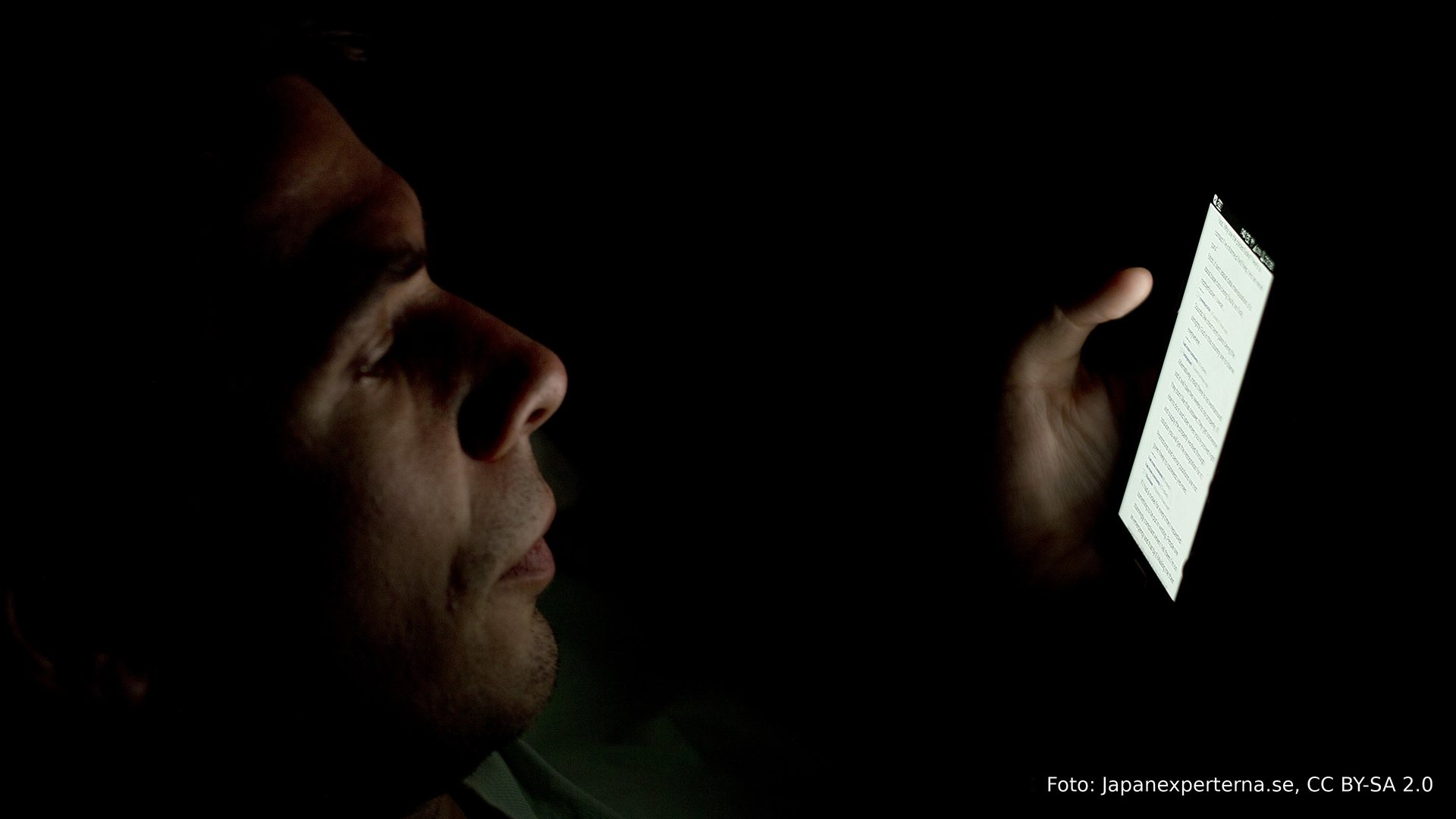Um homem sozinho no escuro, iluminado só pelo celular